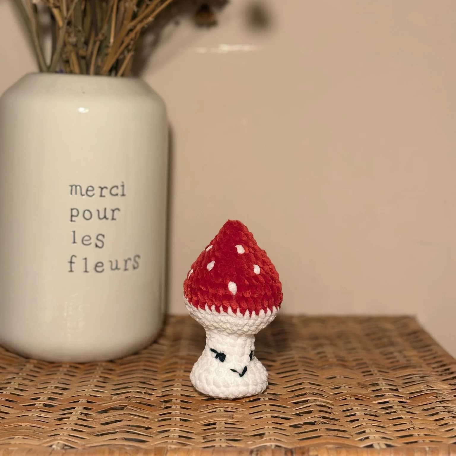 Champignon en peluche crocheté blanc et rouge à pois blancs posé sur un plateau tressé