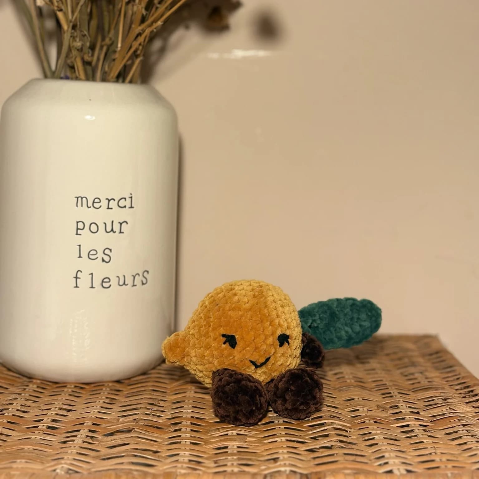 Peluche en laine jaune en forme de citron souriant avec feuille verte, posée sur un meuble en osier.