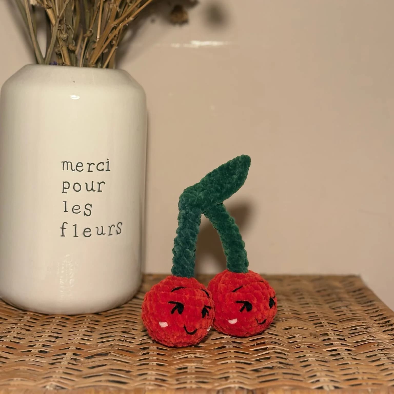 Duo de cerises en laine rouge et tige verte avec visages souriants posé sur de l'osier