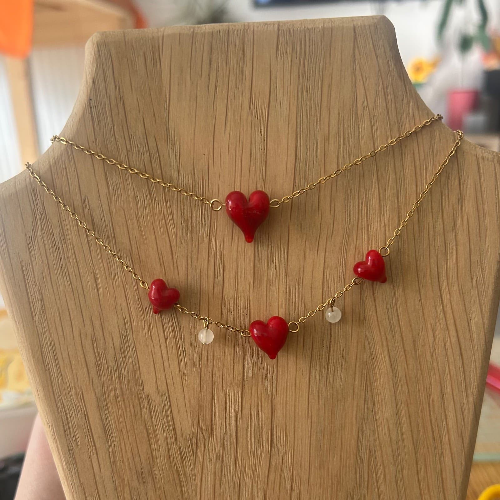 Collier en chaîne dorée orné de cœurs rouges vifs et de perles claires sur un buste en bois