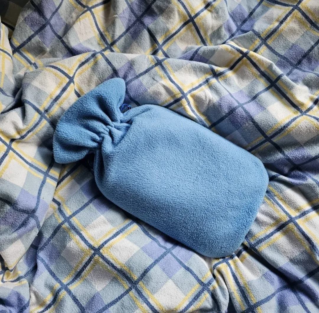 Housse de bouillotte en tissu bleu posée sur un plaid à carreaux.