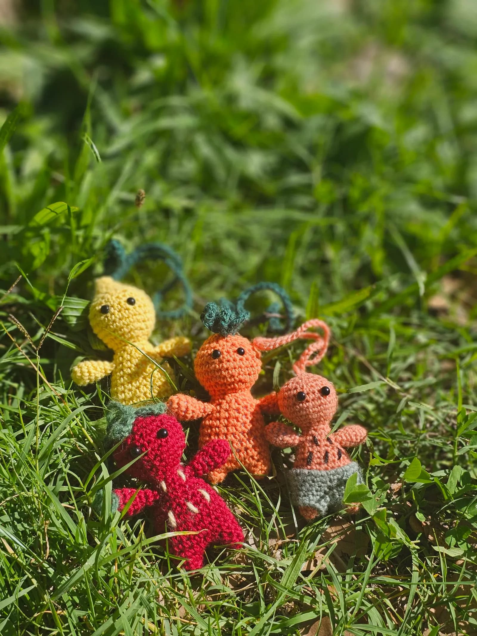 Quatre petites figurines Komsolus au crochet façon fruits posées dans l'herbe ensoleillée
