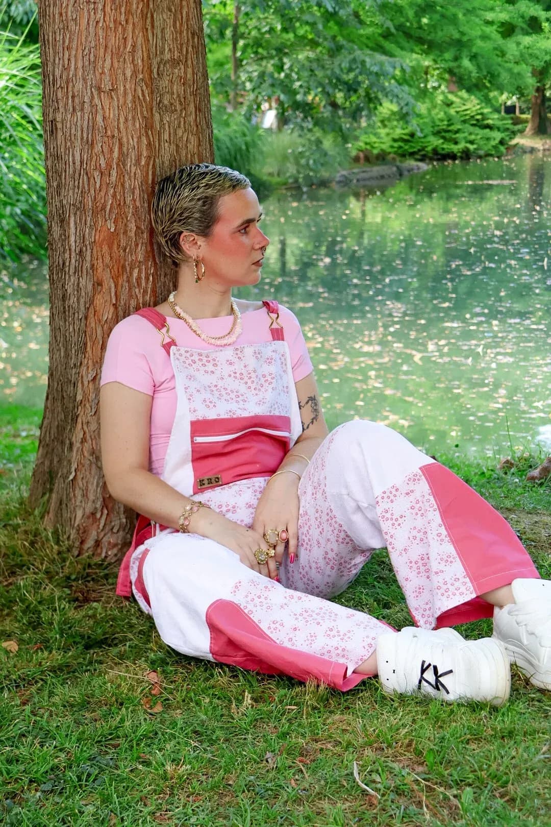 Salopette patchwork rose framboise, blanche et fleurie portée par une personne assise au bord de l'eau.