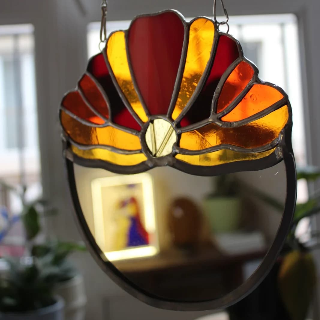 Miroir suspendu surmonté d'un décor en vitrail floral aux reflets orange, rouge et jaune.