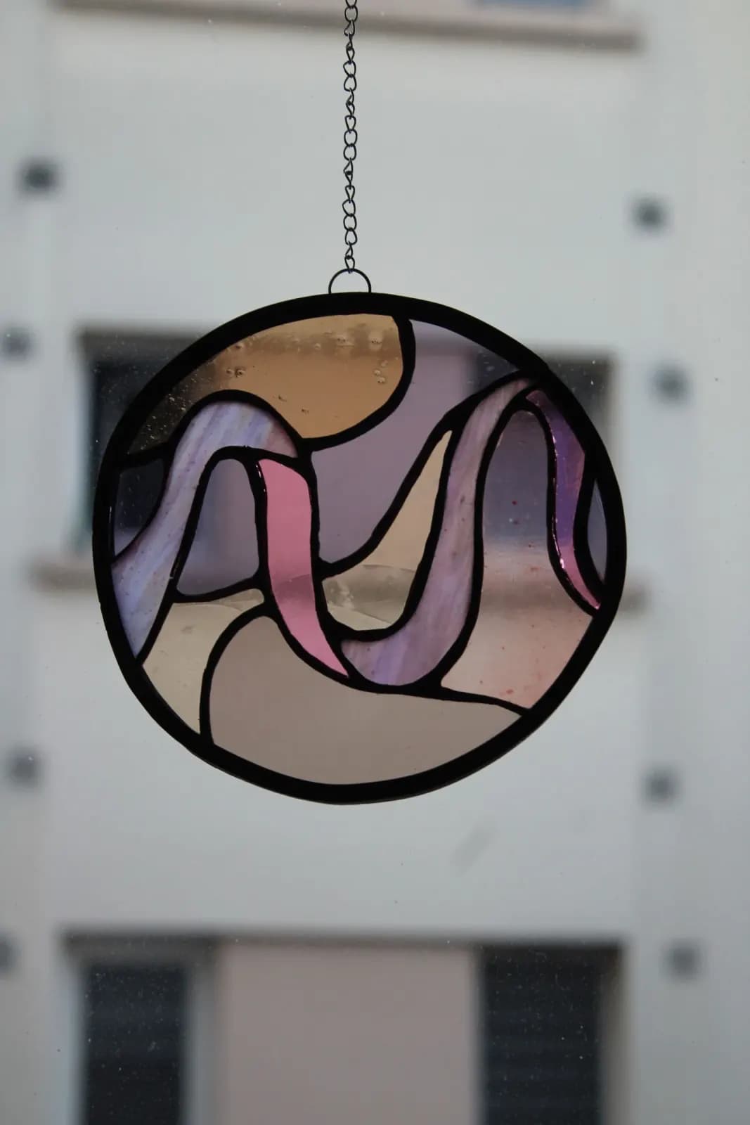 Gros plan sur les reflets holographiques et les verres roses du vitrail circulaire Tiffany.