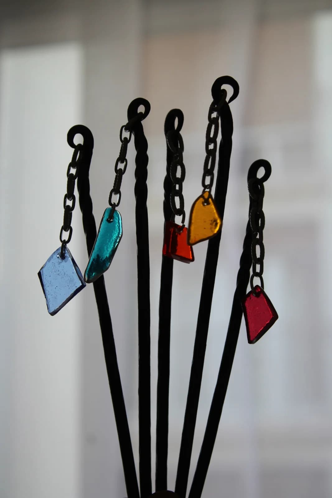 Piques à cheveux en métal noir forgé ornés de pendentifs en verre coloré bleu, jaune et rouge.
