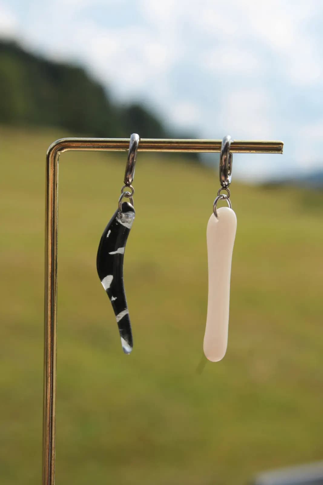 Boucles d'oreilles pendantes asymétriques en verre noir marbré et blanc suspendues à un présentoir.