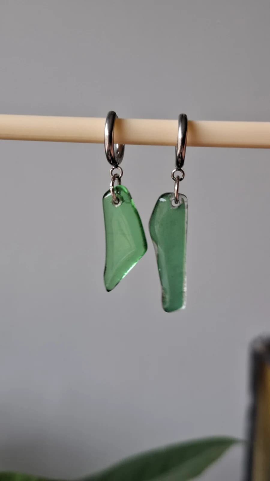 Boucles d'oreilles pendantes en verre vert transparent suspendues sur une tige en bois.