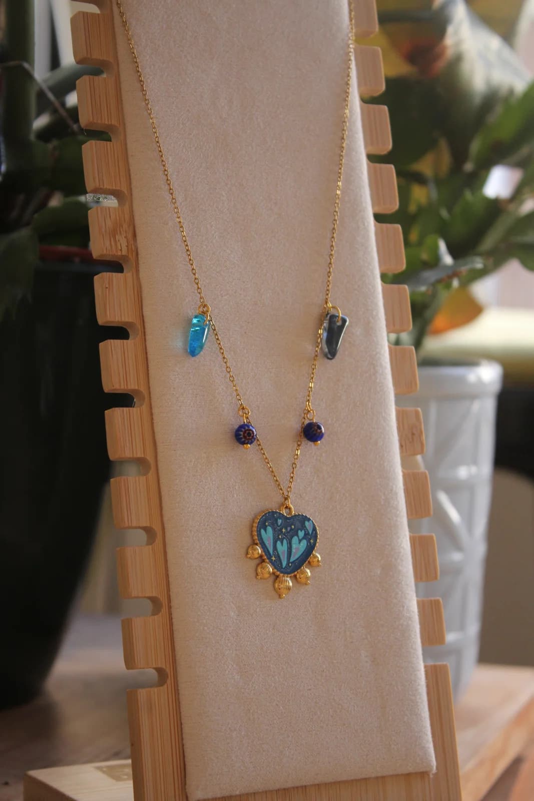 Collier doré avec pendentif cœur bleu et pampilles bleues disposé sur un présentoir en bois.