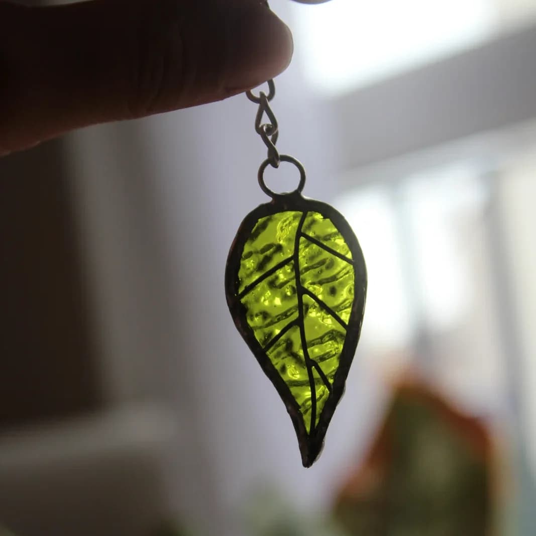 Pendentif feuille en verre texturé vert en transparence à la lumière.