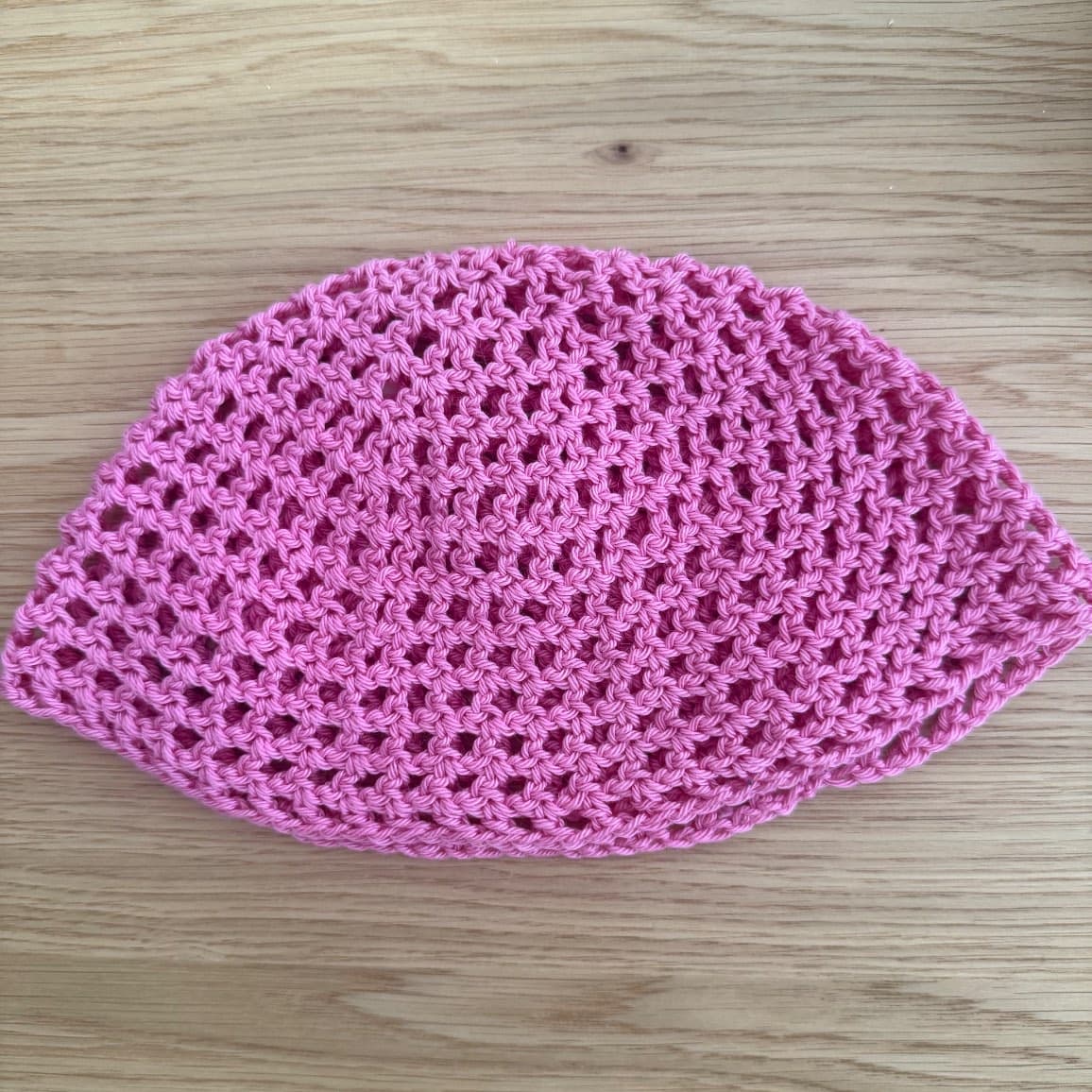 Bonnet ajouré en maille rose posé à plat sur une table en bois