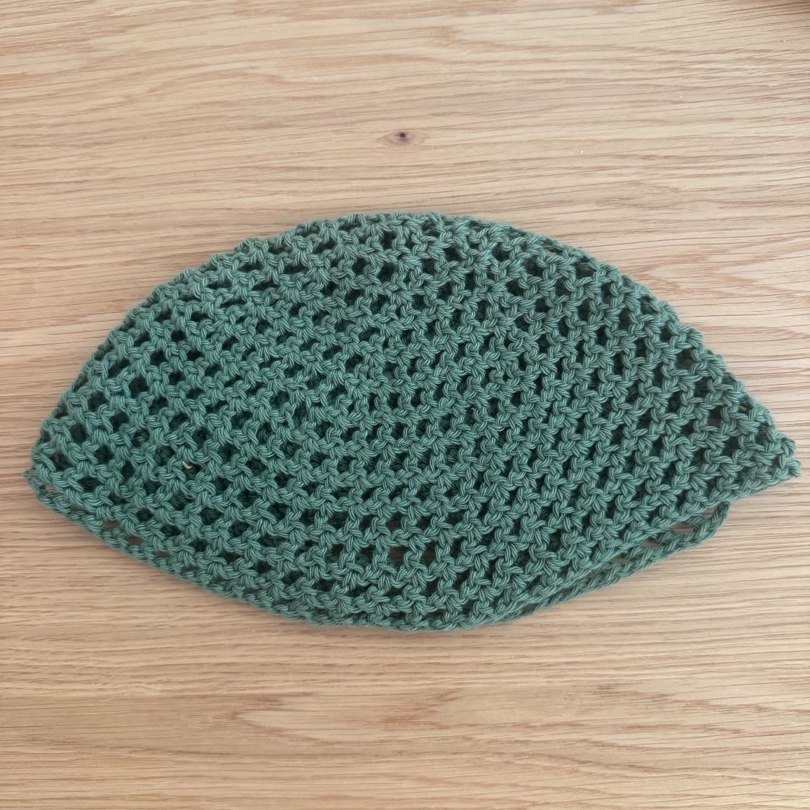 Bonnet ajouré en maille vert posé à plat sur une table en bois clair