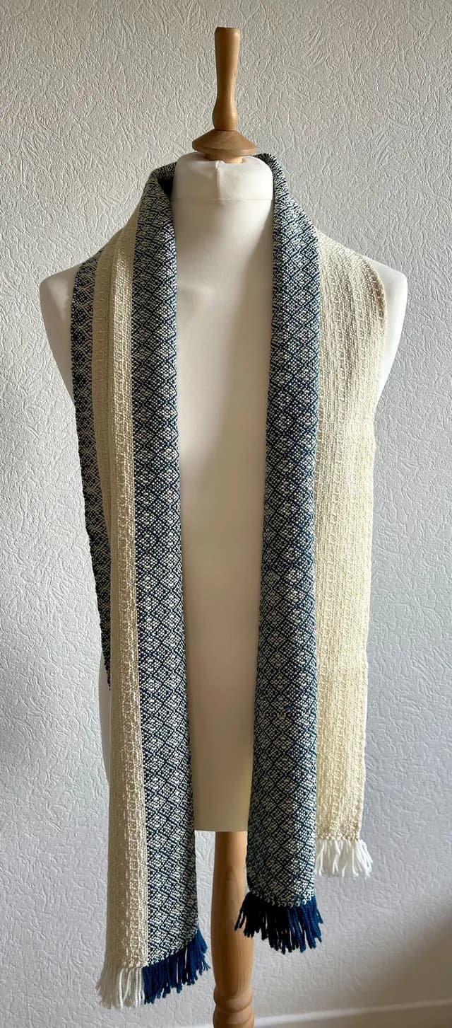 Écharpe tissée bicolore bleu et écru à motifs géométriques et franges, disposée sur un buste de mannequin