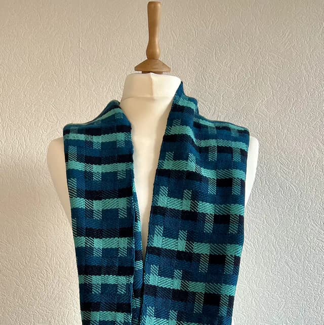Écharpe tissée aux motifs géométriques bleu, canard et noir portée sur un buste de mannequin blanc.