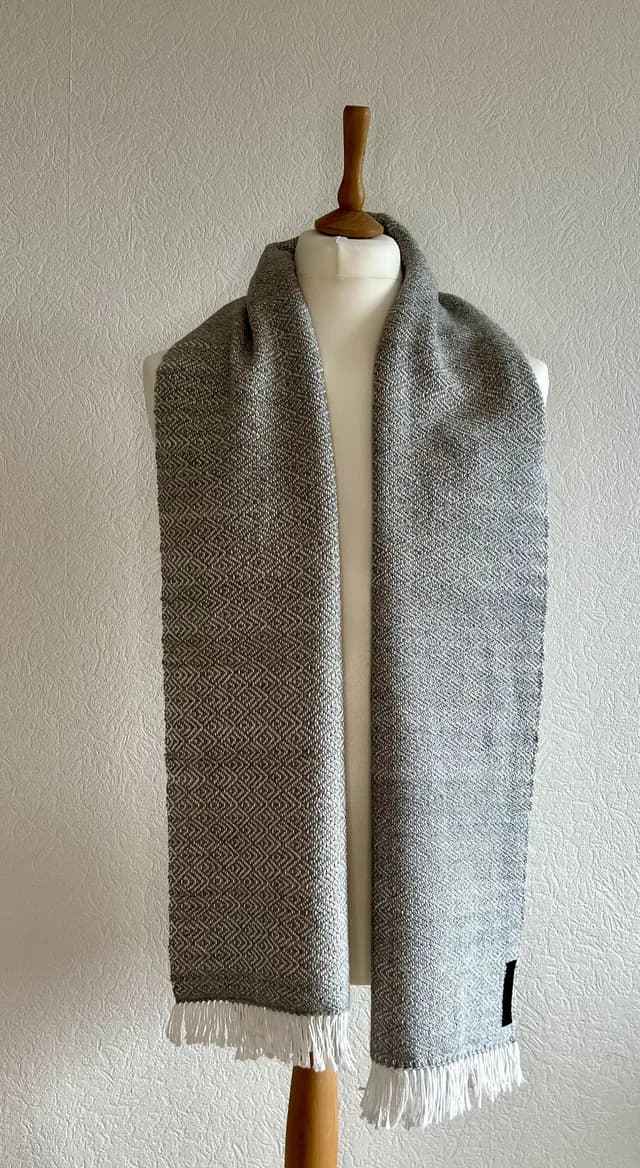 Écharpe tissée grise et blanche à motifs géométriques et franges, présentée sur un buste de couture.
