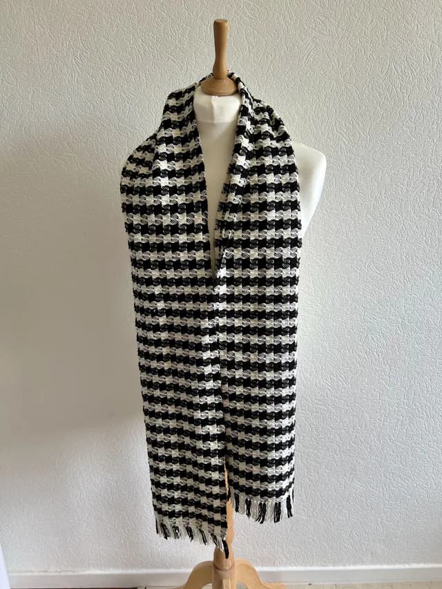 Écharpe tissée noir et blanc à motif géométrique et franges, drapée sur un mannequin de couture.