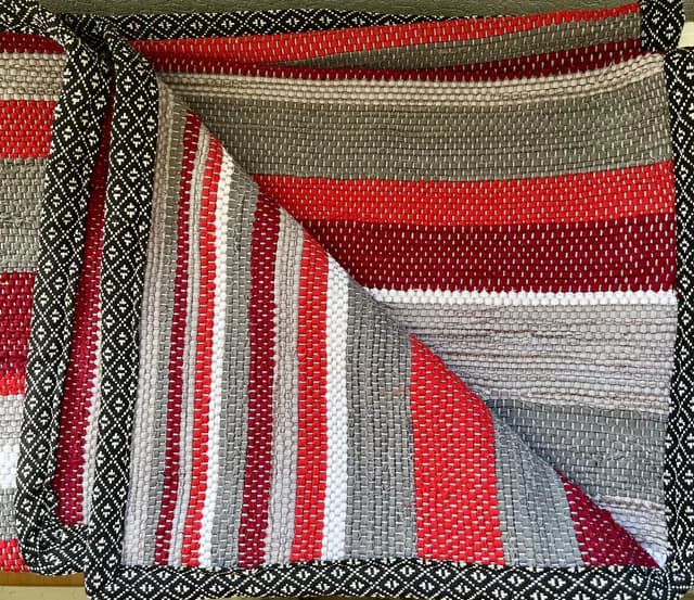 Plaid tissé à rayures rouges, grises et blanches avec liseré à motifs géométriques noirs et blancs