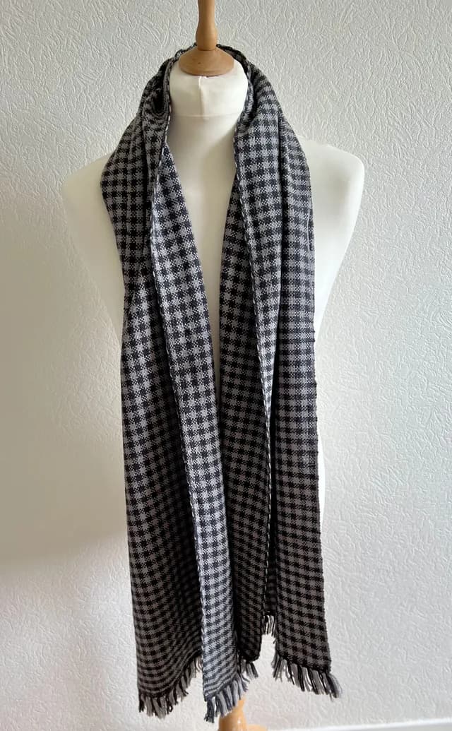 Écharpe tissée à carreaux noirs et gris avec franges, disposée sur un mannequin de couture.