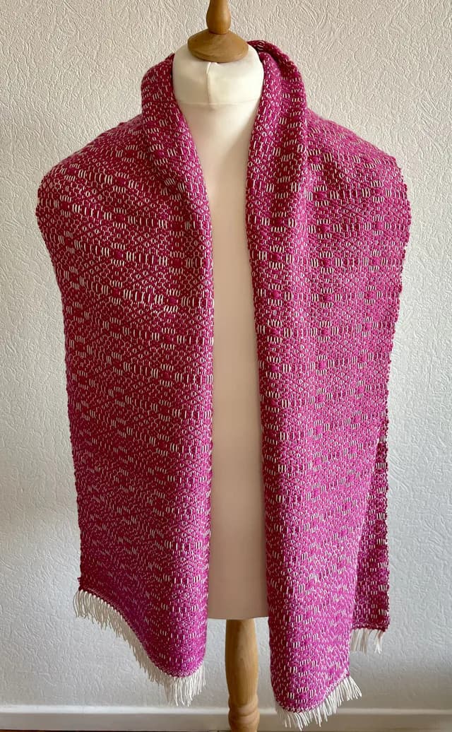 Écharpe tissée rose fuchsia et blanche à franges, drapée sur un buste de mannequin.