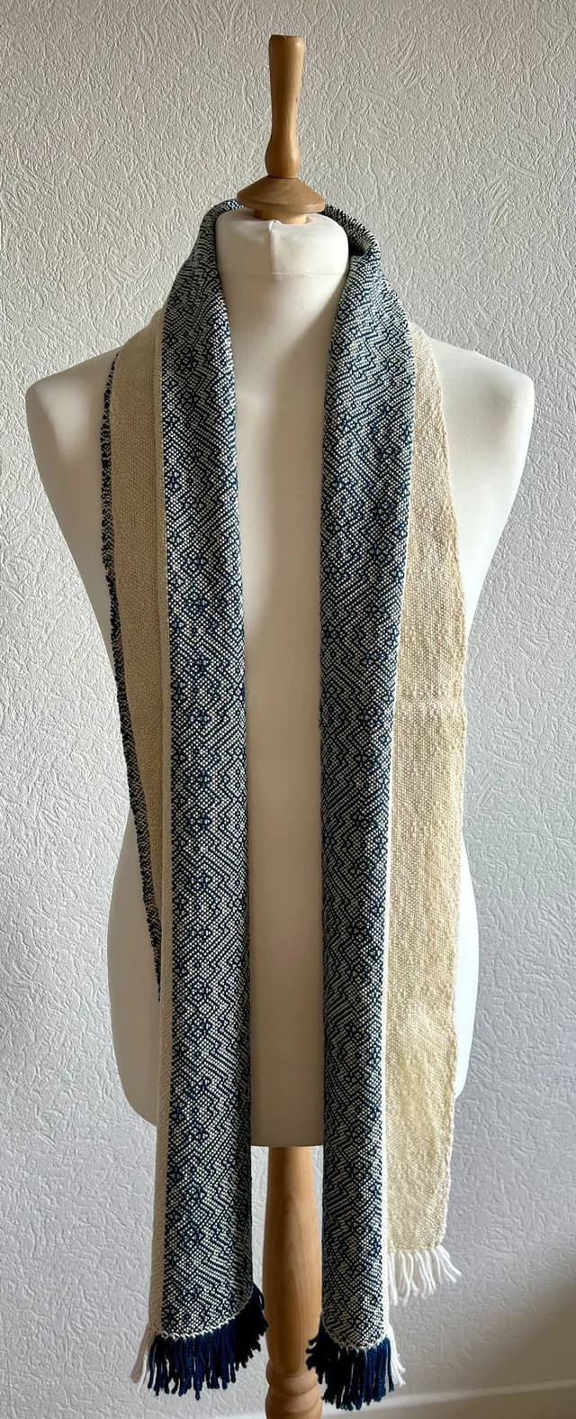 Écharpe bicolore bleu marine et écru à motifs géométriques et franges, disposée sur un buste de mannequin.