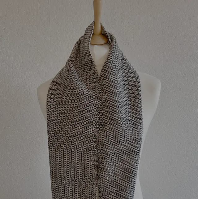 Écharpe tissée noir et blanc à motif géométrique drapée sur un buste de mannequin.