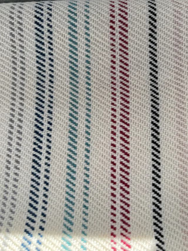 Gros plan sur le tissage champagne, les fines rayures et les franges colorées de l'écharpe en laine.
