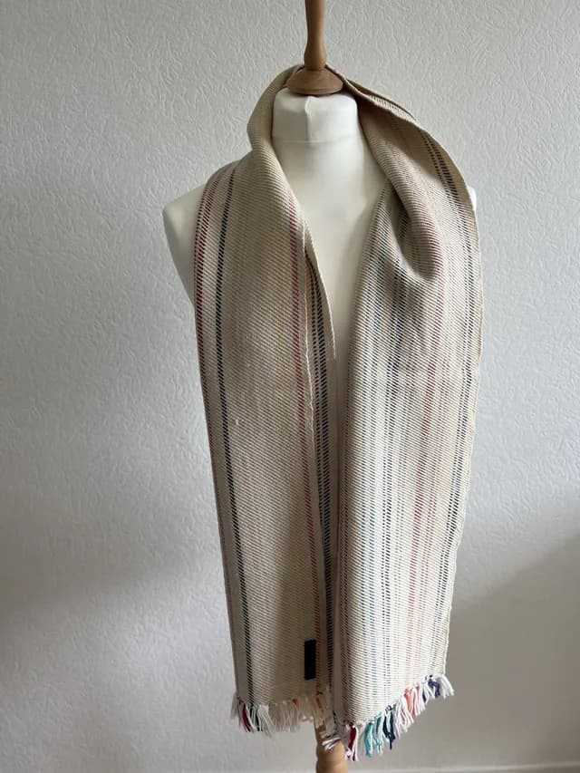 Écharpe champagne à rayures colorées et franges nouées, portée sur un buste de mannequin blanc.