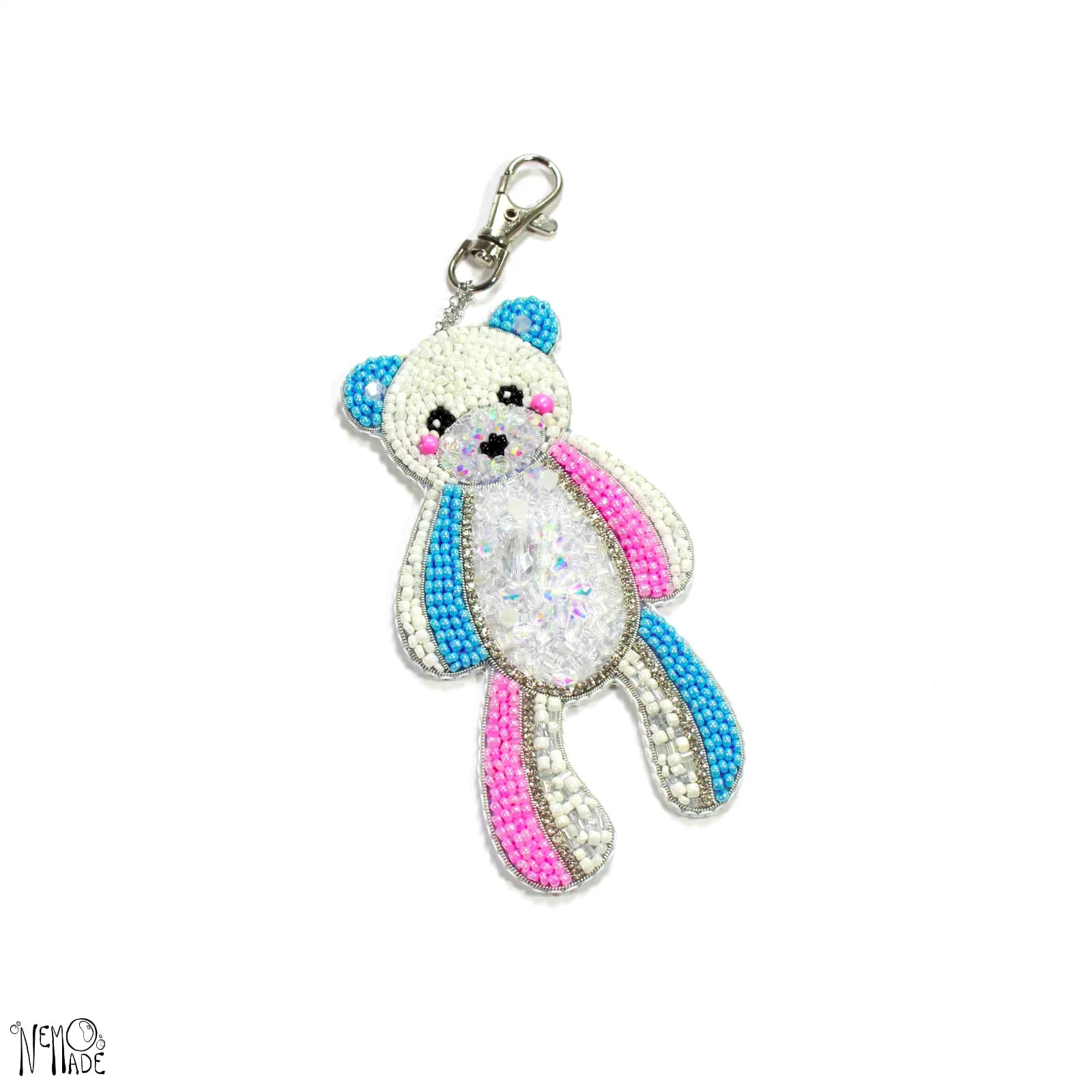 Broche ourson brodée de perles blanches, roses et bleues avec attache mousqueton sur fond blanc.