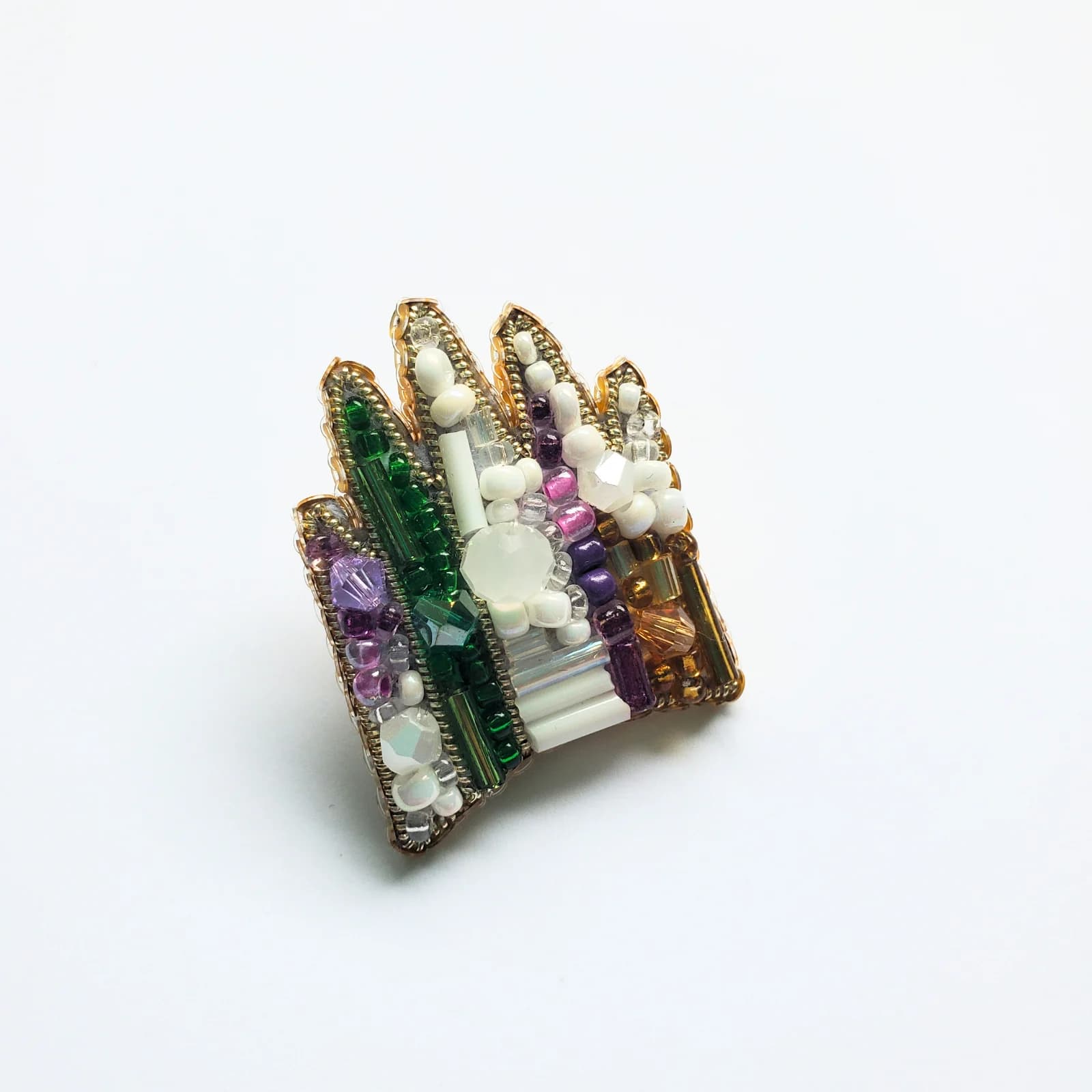 Mini pin en forme de couronne brodé de perles vertes, blanches et violettes sur fond blanc.