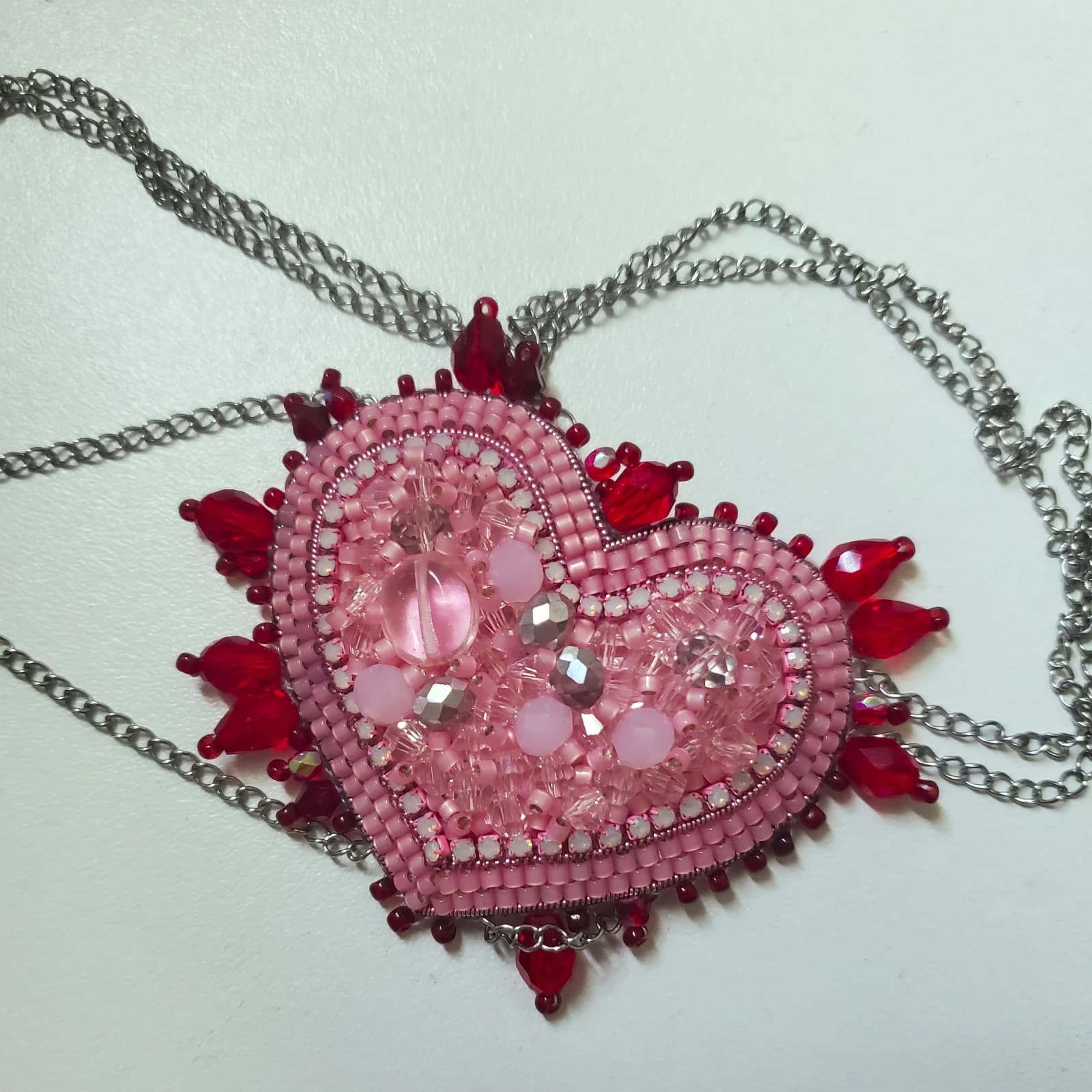 Cache-œil en forme de cœur brodé de perles roses et rouges avec chaînes argentées.