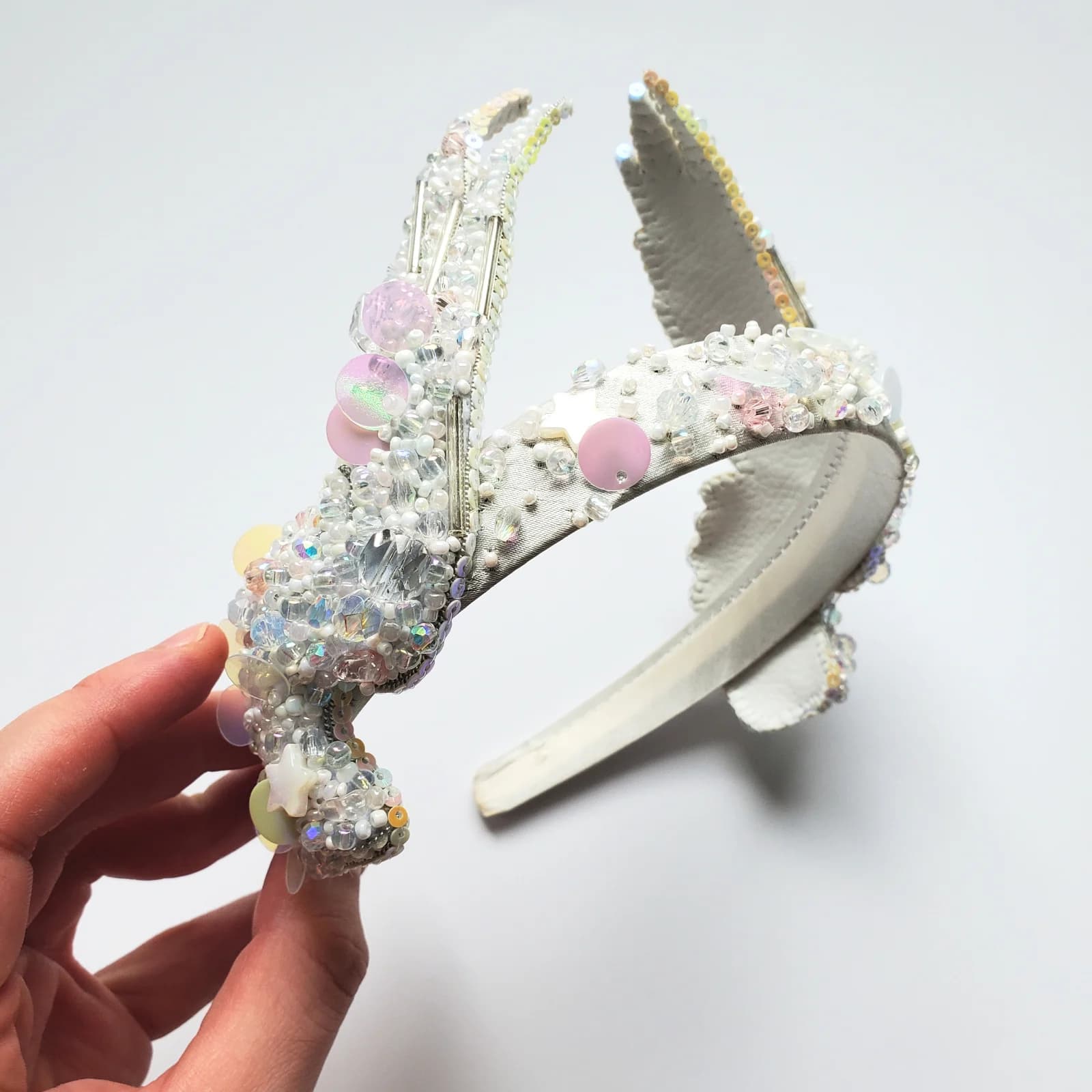 Serre-tête blanc orné de perles et sequins pastel tenu en main sur fond blanc