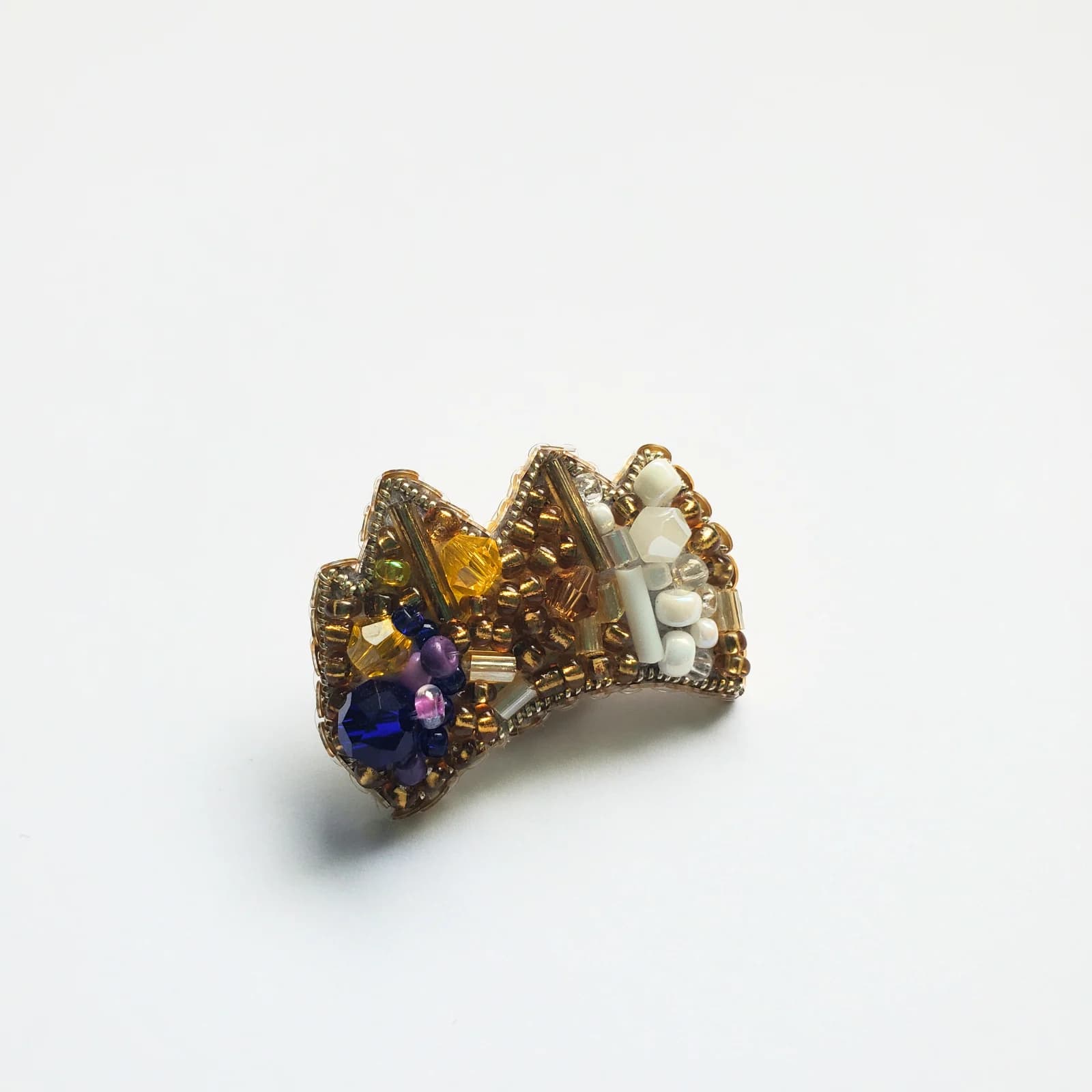 Mini pin en forme de couronne orné de perles dorées, blanches et bleues sur fond blanc.