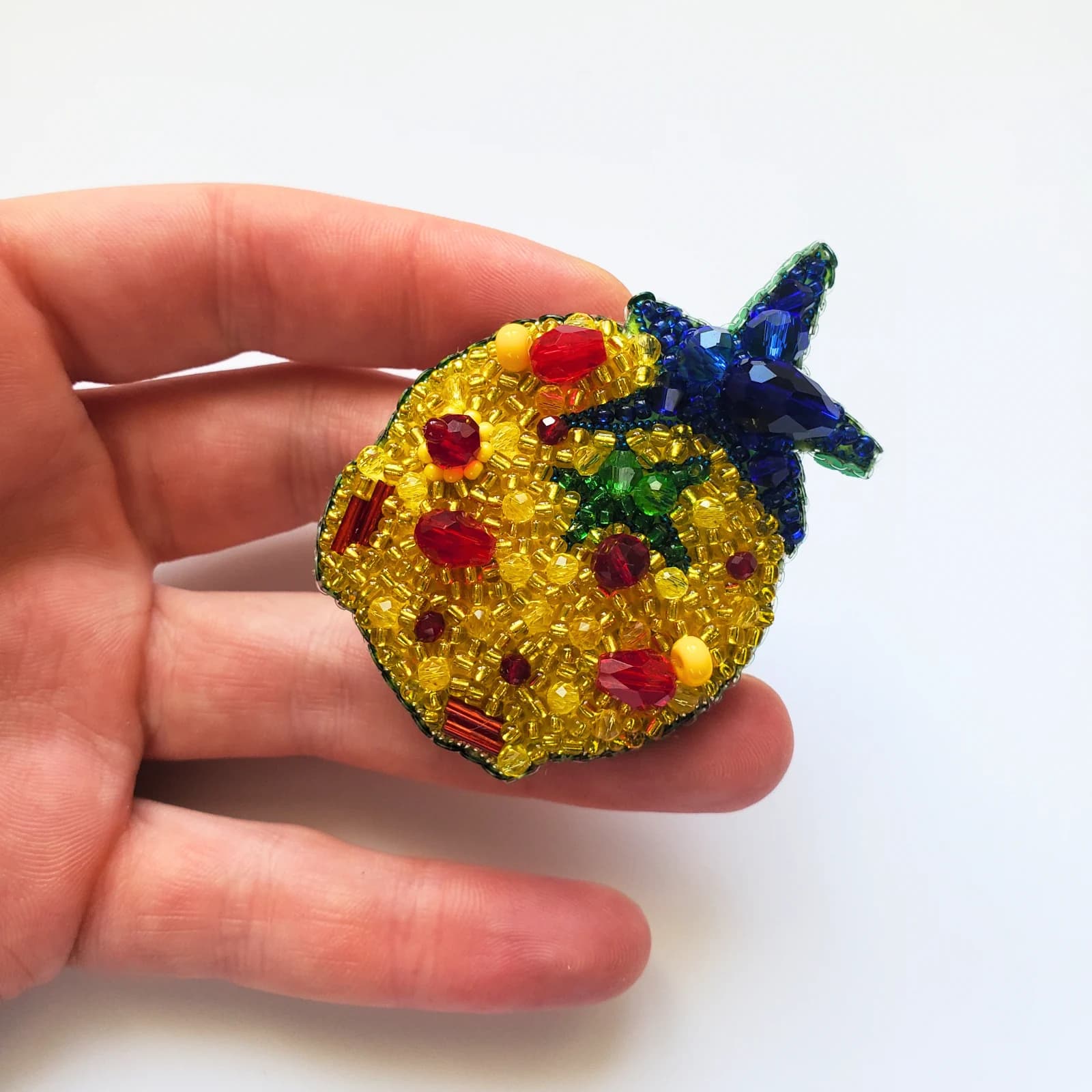 Broche perlée ronde Astéroïde B612 jaune et bleue tenue dans la main sur fond blanc.
