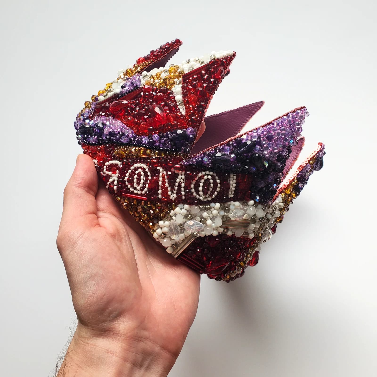 Couronne TOMORROW tenue en main, ornée de broderies perlées rouges, violettes et blanches.