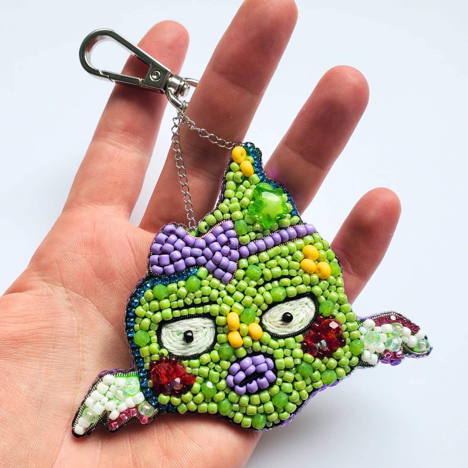 Porte-clé SMILE brodé en perles vertes et mauves avec mousqueton, tenu dans une main.