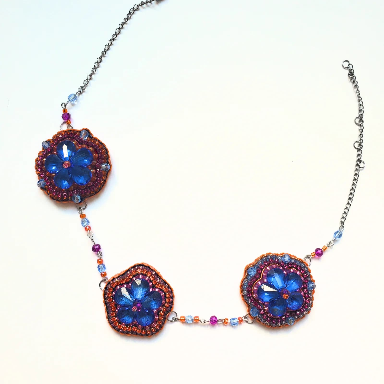 Collier avec trois médaillons floraux brodés de perles bleues sur chaîne argentée, vue d'ensemble.