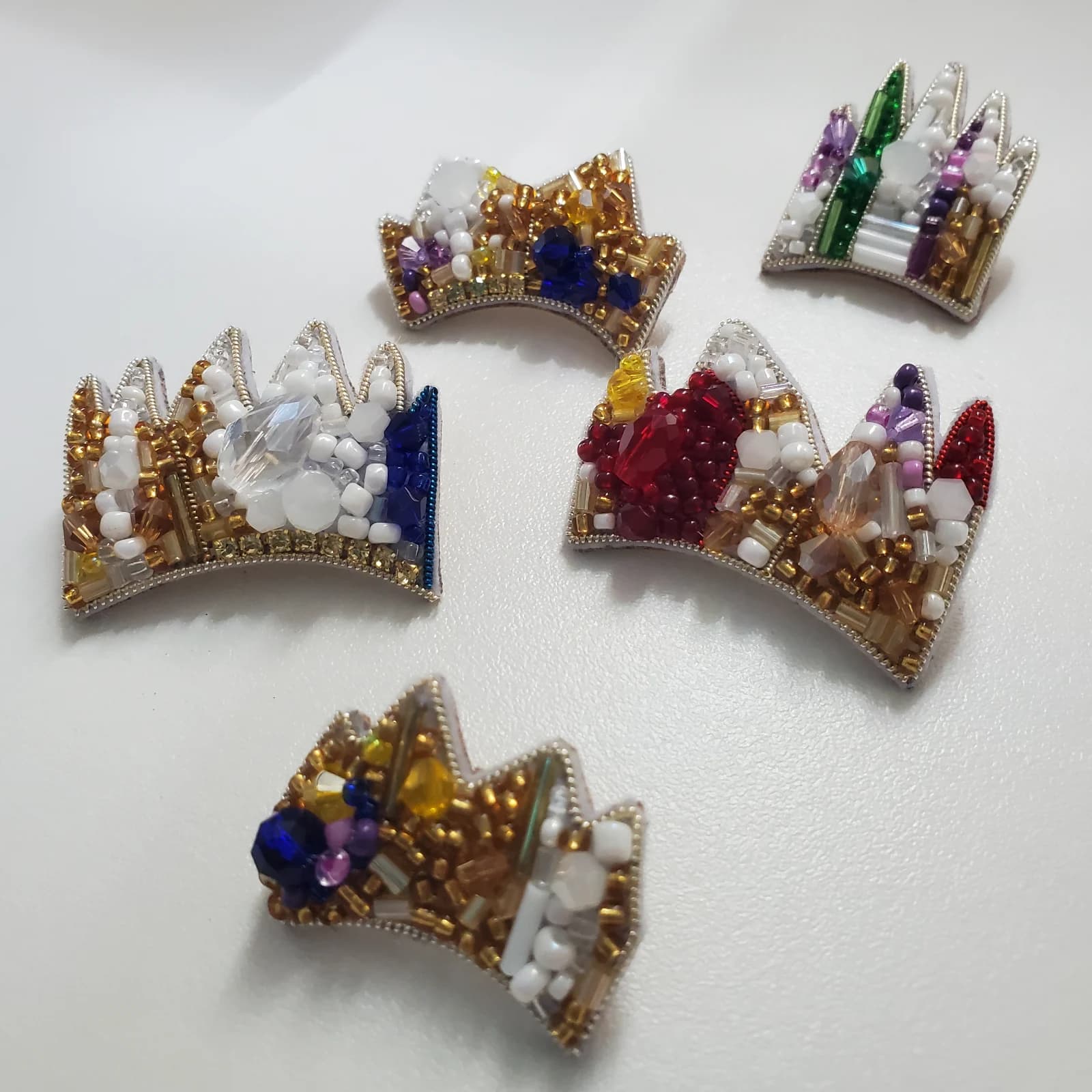Cinq pin's en forme de couronne brodés de perles multicolores et cannetille dorée