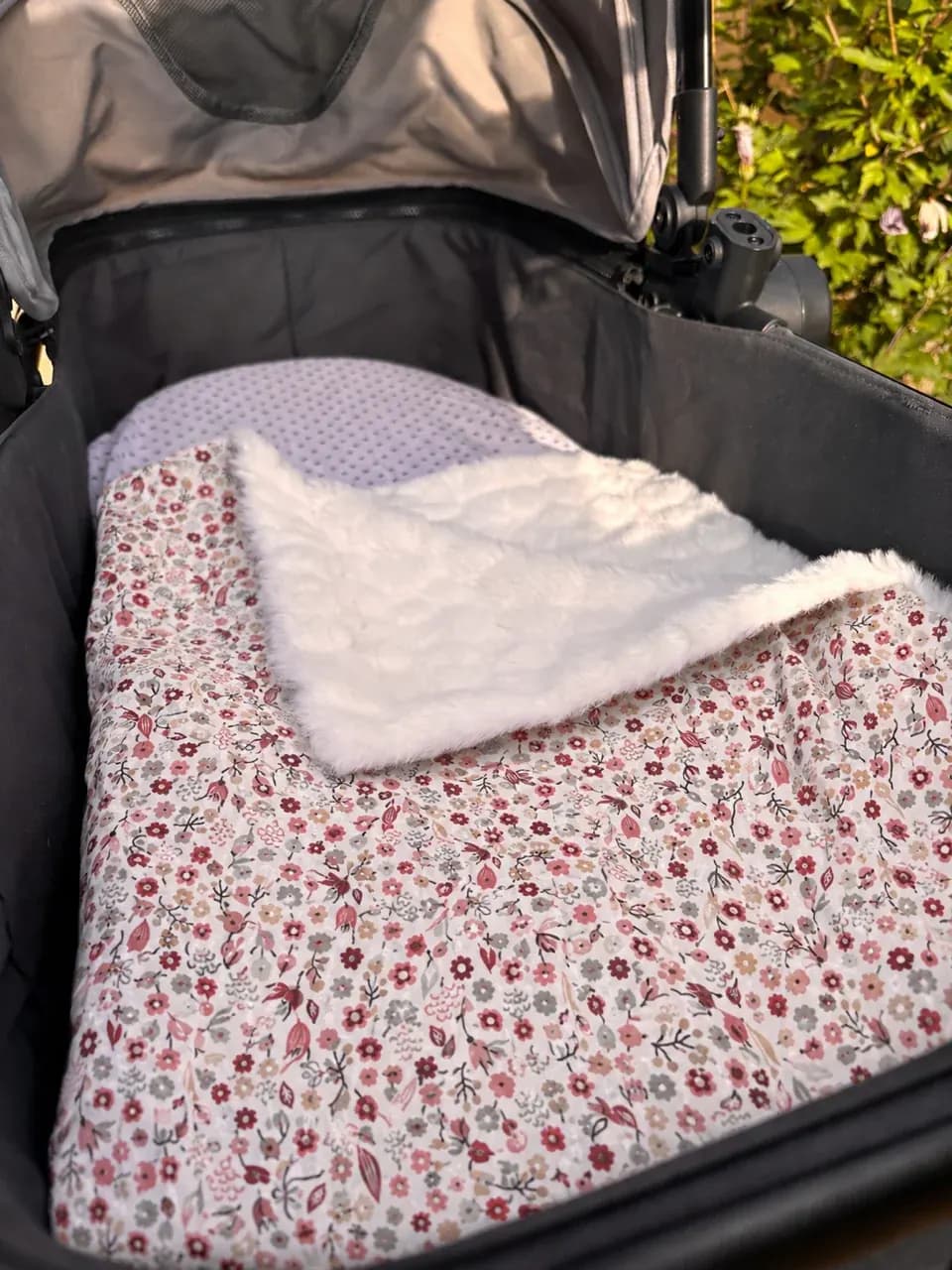 Couverture pour bébé à motif floral posée dans un landau avec revers en polaire texturée blanche.