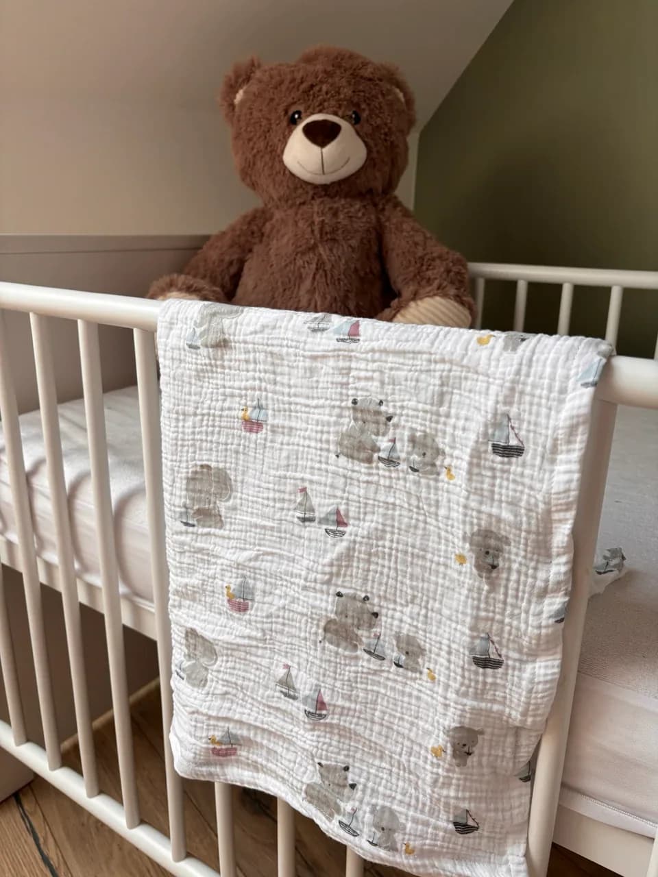 Lange en gaze de coton blanche à motifs bateaux et oursons, posé sur la barrière d'un lit de bébé.