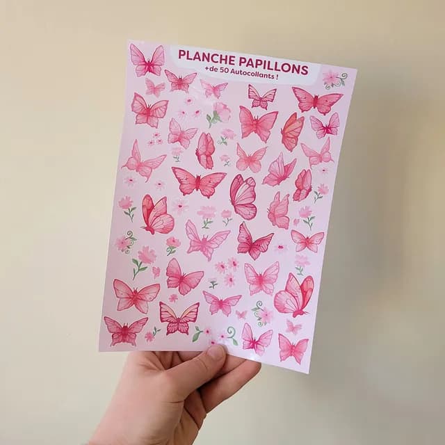 Planche d'autocollants tenue en main présentant de nombreux motifs de papillons roses illustrés.