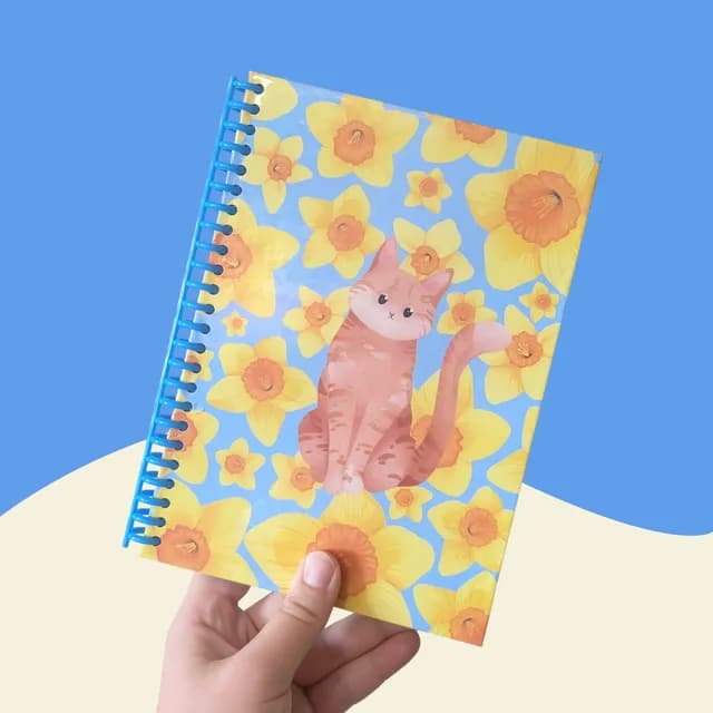 Carnet à spirale bleue A5 illustré d'un chat roux parmi des fleurs jaunes sur fond bleu clair.