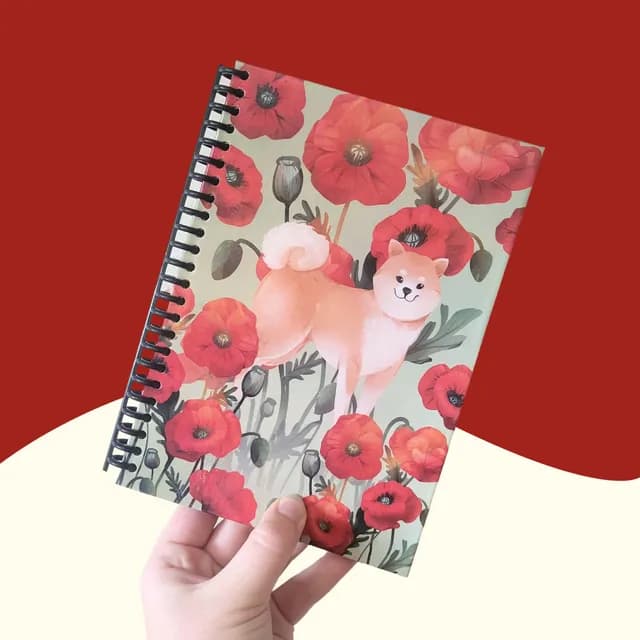 Carnet A5 à spirale tenu en main, illustré d'un chien Shiba entouré de coquelicots rouges