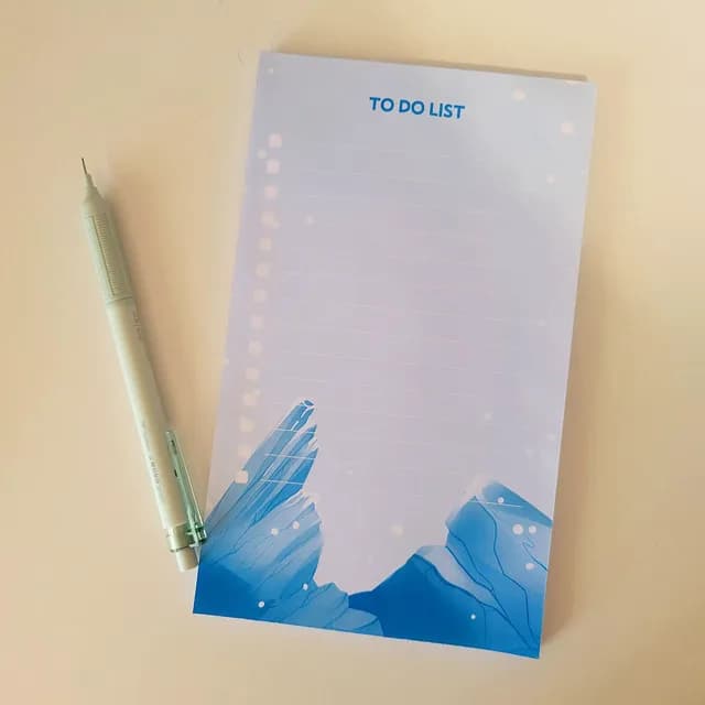 Bloc-notes to-do list illustré de glaciers bleus avec lignes d'écriture, posé à côté d'un crayon.