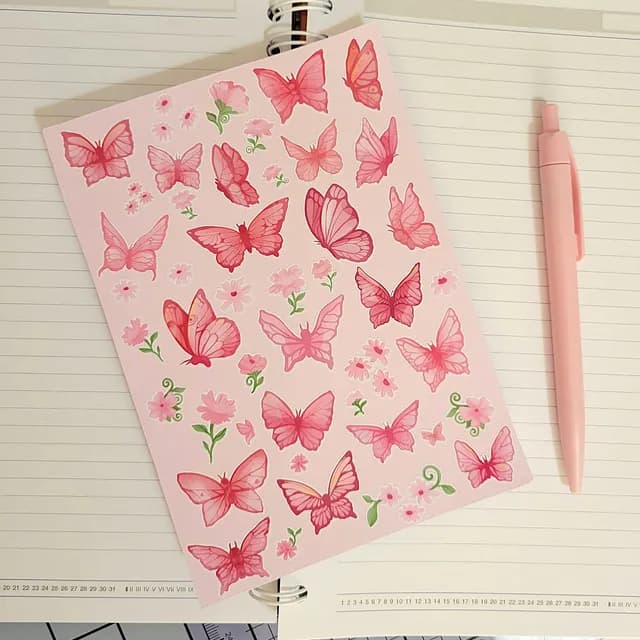 Planche de stickers avec papillons et fleurs roses posée sur un carnet avec un stylo