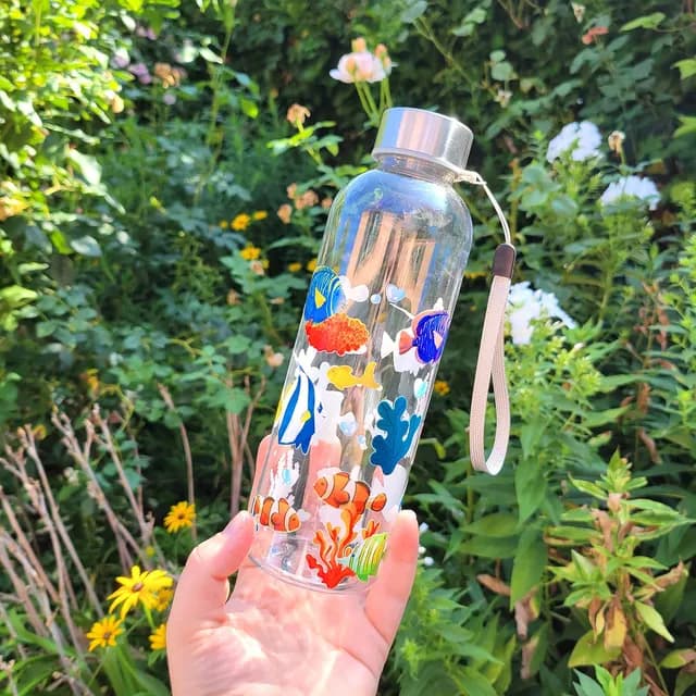 Main tenant une gourde transparente ornée de poissons et coraux colorés en extérieur