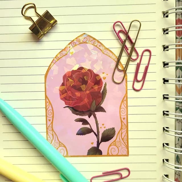Sticker ogive à reflets holographiques représentant une rose rouge, posé sur les pages d'un carnet