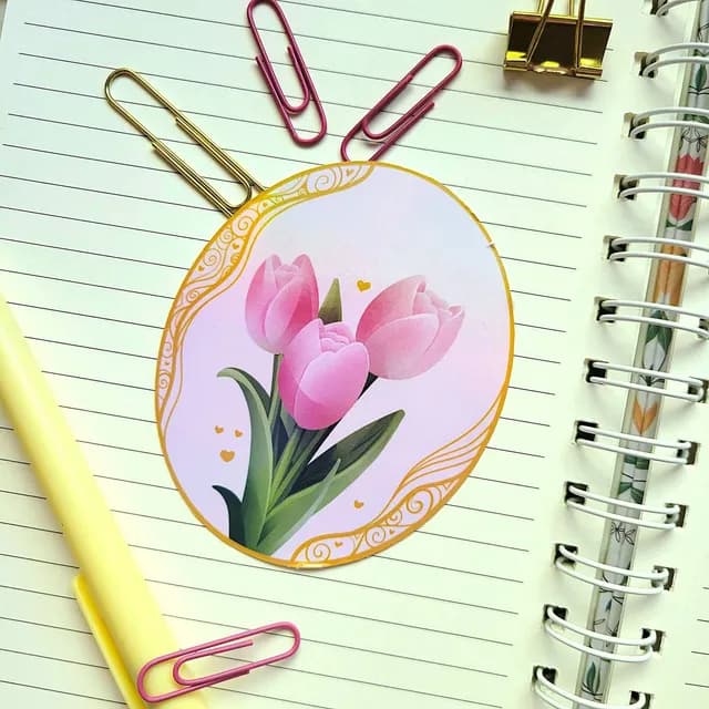 Sticker ovale orné de tulipes roses et bordure dorée, posé sur les pages d'un carnet à spirale.