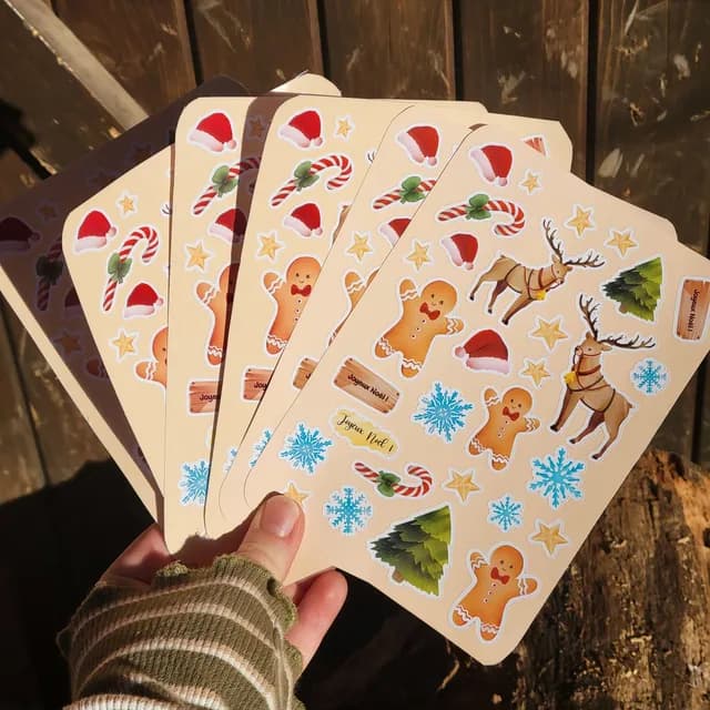 Main tenant en éventail plusieurs planches d'autocollants aux motifs festifs de Noël.