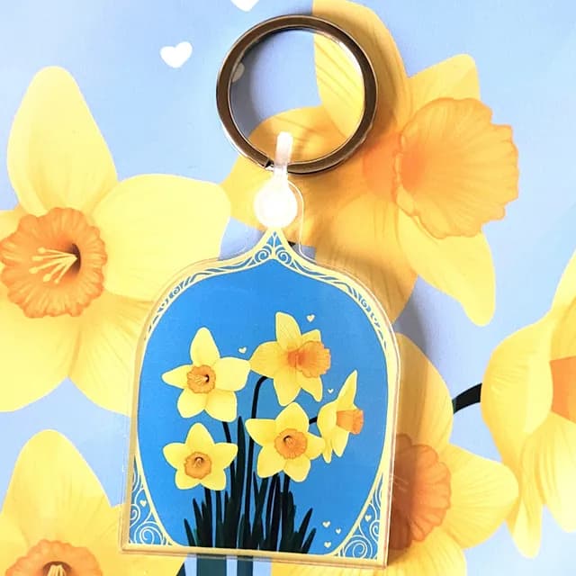 Porte-clés en forme d'arche illustré de jonquilles jaunes sur fond bleu ciel avec attache métallique.
