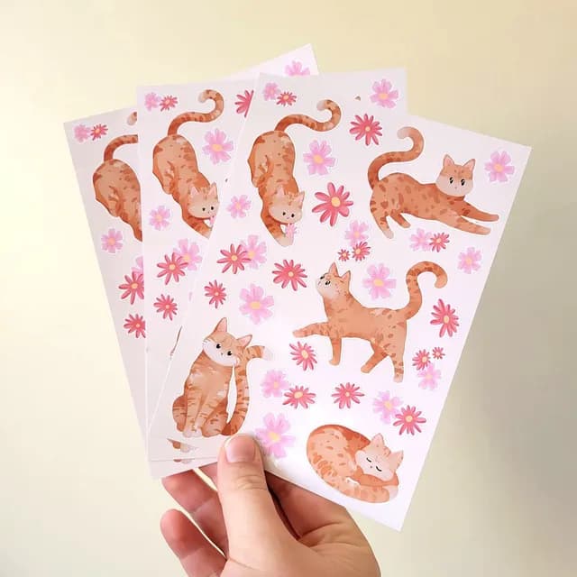 Vue d'ensemble de la planche d'autocollants illustrés de chats roux tigrés et petites fleurs roses.